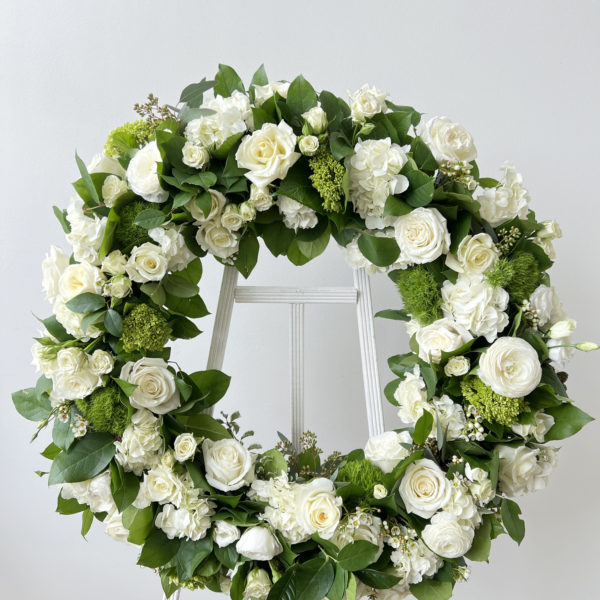 floral sympathy wreath of white blooms and greenery on white easel