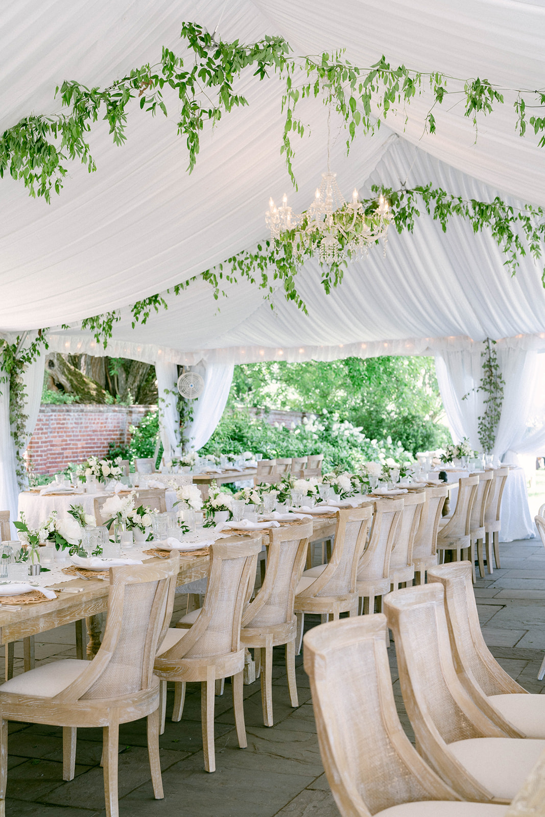 elegant wedding setup under tent with fancy chairs, florals, chandeliers, and ivy hung from tent